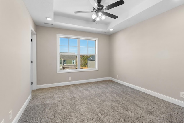 carpeted spare room with a tray ceiling and ceiling fan