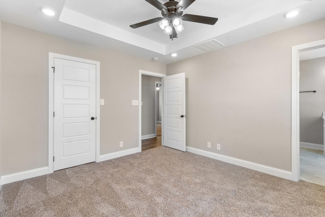 unfurnished bedroom with carpet, a raised ceiling, and ceiling fan