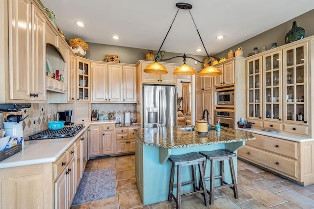 kitchen featuring a kitchen island with sink, light brown cabinets, stainless steel appliances, and decorative light fixtures