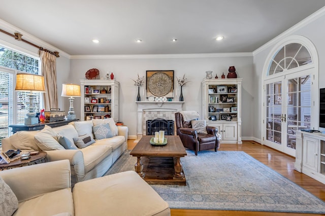 living room with a tiled fireplace, ornamental molding, french doors, and light hardwood / wood-style flooring