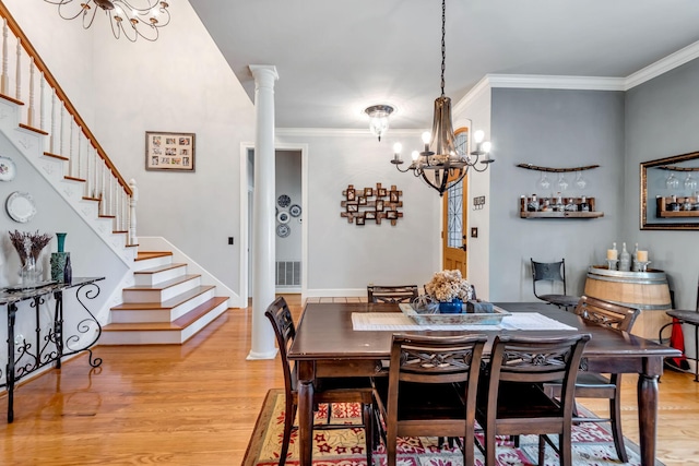 dining area with light wood-type flooring, ornate columns, a notable chandelier, and crown molding