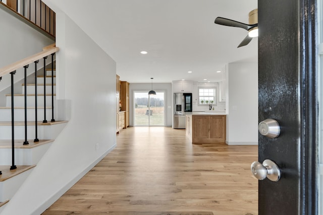 kitchen featuring stainless steel refrigerator with ice dispenser, hanging light fixtures, light wood-type flooring, ceiling fan, and white cabinets