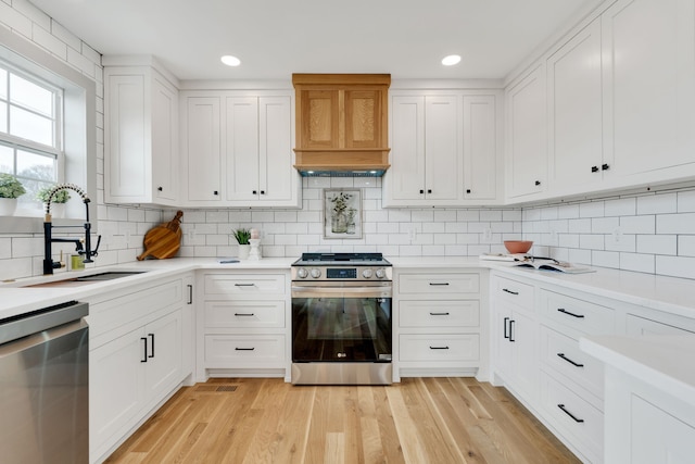 kitchen featuring tasteful backsplash, white cabinetry, sink, light hardwood / wood-style floors, and stainless steel appliances