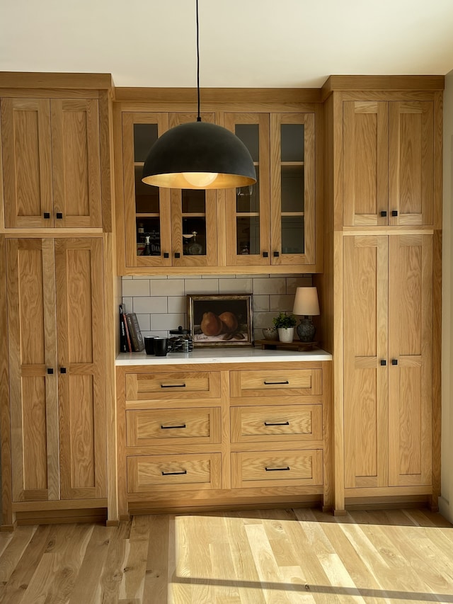 kitchen with decorative light fixtures, light hardwood / wood-style floors, and backsplash