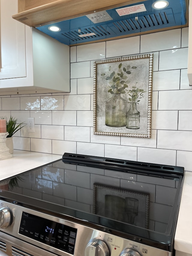 room details featuring white cabinetry, ventilation hood, stainless steel range oven, and backsplash