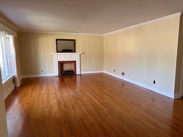 unfurnished living room featuring ornamental molding, dark wood-type flooring, and a brick fireplace