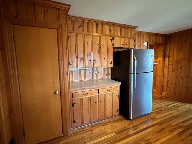 kitchen with wooden walls, stainless steel fridge, and light wood-type flooring