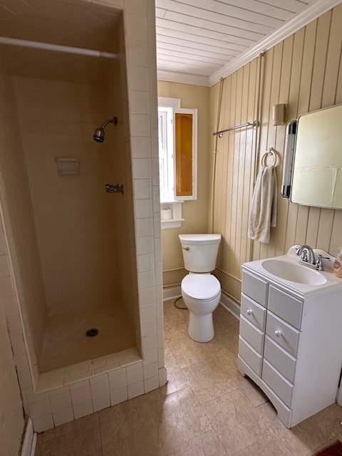 bathroom with tile floors, toilet, vanity, crown molding, and a tile shower