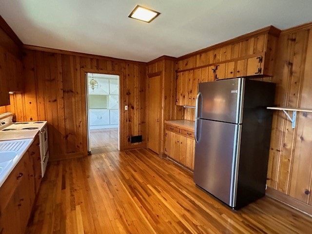 kitchen with white range with electric cooktop, light wood-type flooring, wood walls, and stainless steel fridge