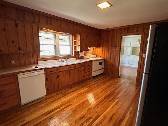 kitchen with white appliances, wood walls, light hardwood / wood-style floors, and sink