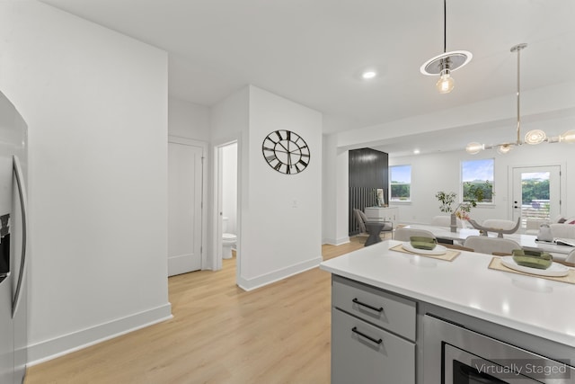 kitchen with hanging light fixtures, gray cabinetry, light wood-type flooring, and stainless steel appliances