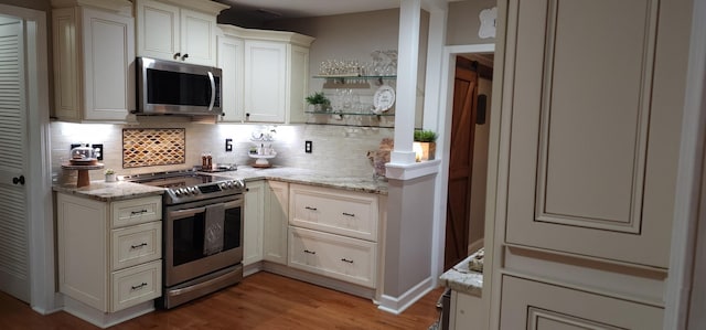 kitchen with light hardwood / wood-style floors, backsplash, light stone counters, and stainless steel appliances