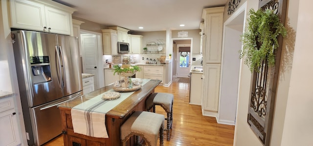 kitchen with light stone countertops, stainless steel appliances, light hardwood / wood-style flooring, and tasteful backsplash