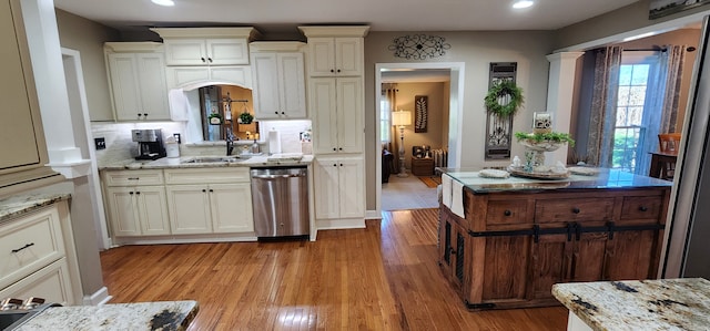 kitchen with cream cabinetry, light hardwood / wood-style flooring, dishwasher, light stone countertops, and sink