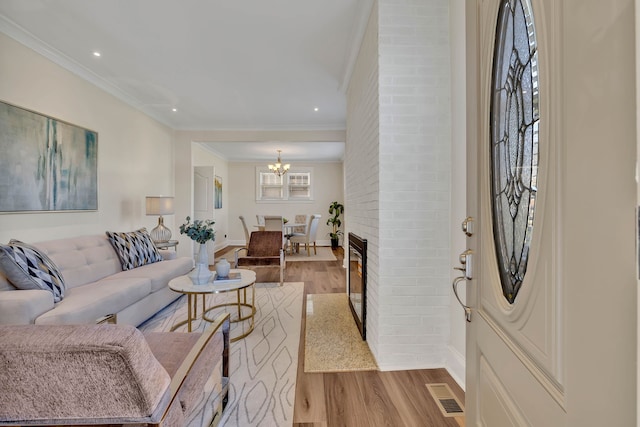 living room featuring light wood-type flooring, ornamental molding, and a brick fireplace