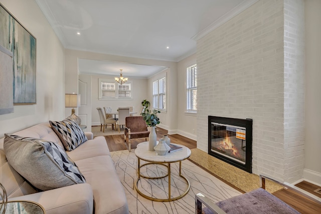 living room featuring a large fireplace, light hardwood / wood-style floors, ornamental molding, and a chandelier