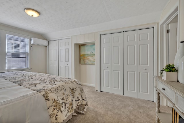 bedroom featuring multiple closets, an AC wall unit, vaulted ceiling, a textured ceiling, and light carpet