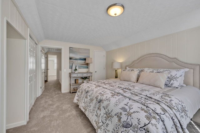 bedroom with a closet, light colored carpet, a textured ceiling, and vaulted ceiling