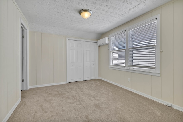 unfurnished bedroom with a wall mounted AC, light carpet, a closet, and a textured ceiling