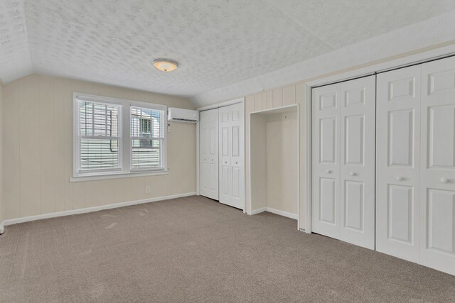 unfurnished bedroom featuring light carpet, two closets, a wall mounted AC, and lofted ceiling