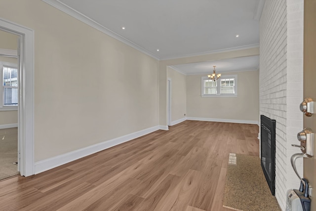 unfurnished living room with crown molding, light wood-type flooring, a notable chandelier, and a brick fireplace