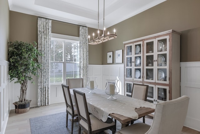 dining area featuring a notable chandelier, a raised ceiling, light wood-type flooring, and crown molding