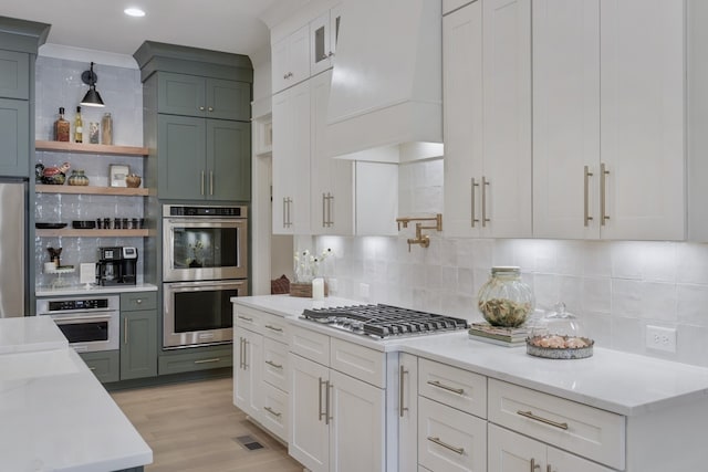 kitchen featuring white cabinetry, stainless steel appliances, premium range hood, decorative light fixtures, and decorative backsplash