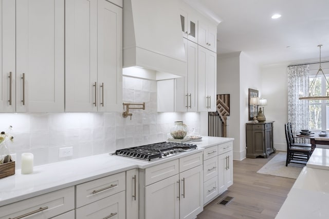 kitchen with decorative backsplash, light stone countertops, decorative light fixtures, light hardwood / wood-style floors, and white cabinetry