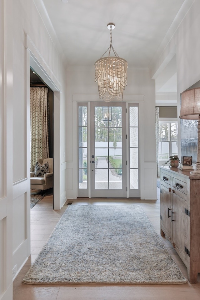 entryway with light wood-type flooring, crown molding, and an inviting chandelier