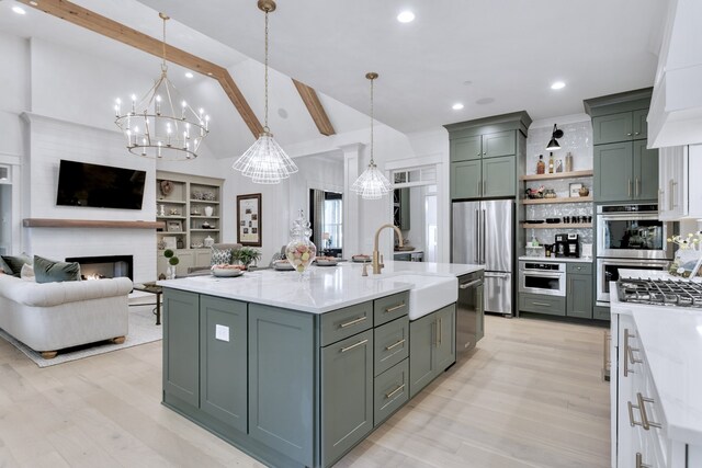 kitchen featuring stainless steel appliances, pendant lighting, a center island with sink, built in features, and a fireplace