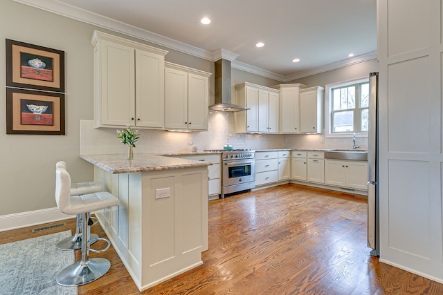 kitchen featuring high end stove, hardwood / wood-style floors, a breakfast bar, light stone countertops, and wall chimney exhaust hood