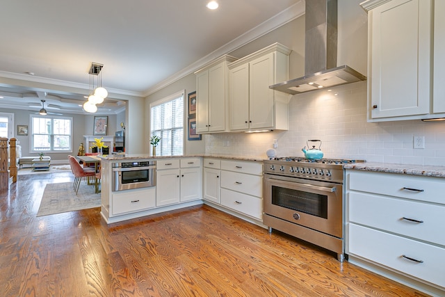 kitchen featuring stainless steel appliances, light hardwood / wood-style flooring, pendant lighting, ceiling fan, and wall chimney range hood