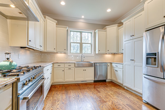 kitchen with appliances with stainless steel finishes, tasteful backsplash, wall chimney exhaust hood, and light hardwood / wood-style floors