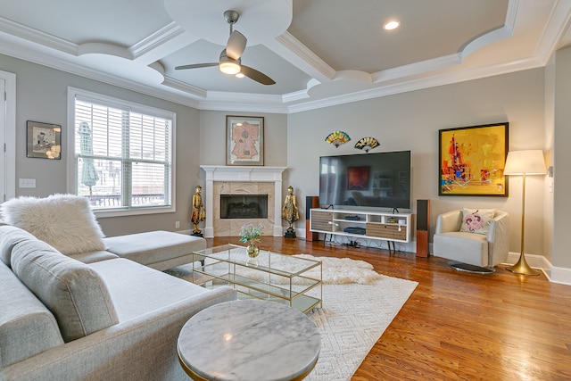 living room featuring wood-type flooring, ceiling fan, coffered ceiling, a tile fireplace, and ornamental molding