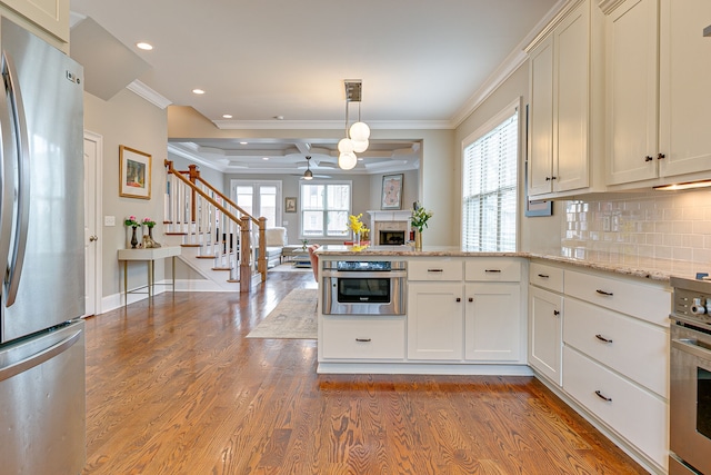 kitchen featuring wood-type flooring, stainless steel appliances, pendant lighting, tasteful backsplash, and ornamental molding