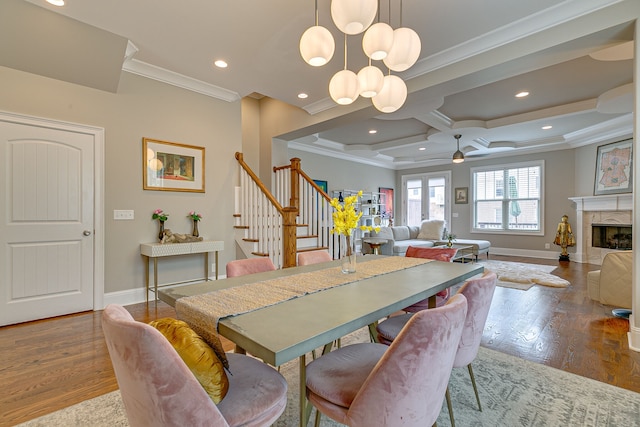 dining area with coffered ceiling, a fireplace, light hardwood / wood-style floors, and ceiling fan with notable chandelier