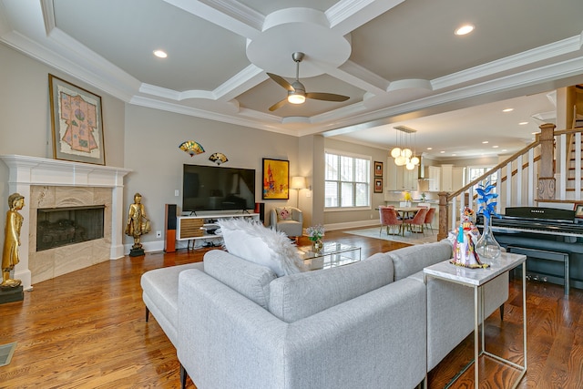 living room featuring hardwood / wood-style floors, coffered ceiling, ceiling fan with notable chandelier, a fireplace, and ornamental molding