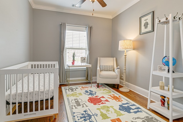 bedroom featuring ceiling fan, crown molding, hardwood / wood-style floors, and a nursery area