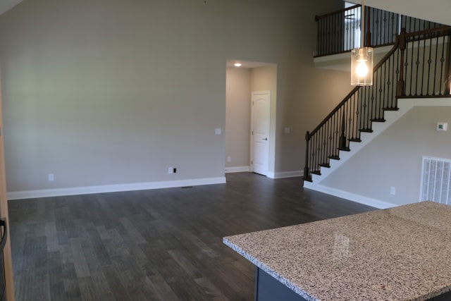 unfurnished living room with dark hardwood / wood-style flooring and a towering ceiling