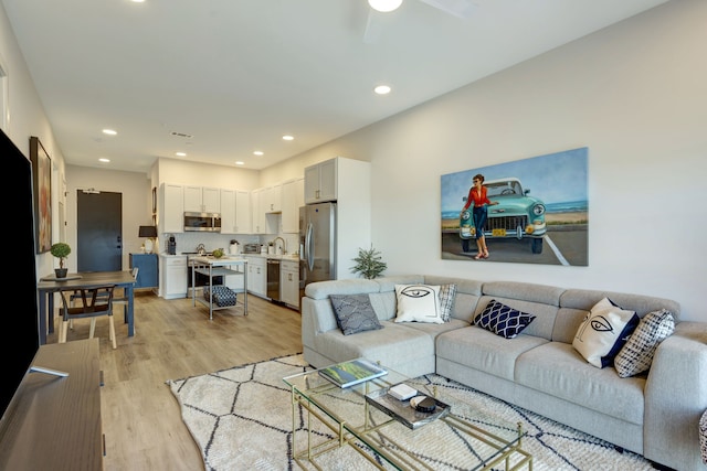 living room with light hardwood / wood-style floors, ceiling fan, and sink