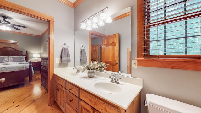 bathroom with toilet, ceiling fan, double sink vanity, crown molding, and hardwood / wood-style flooring