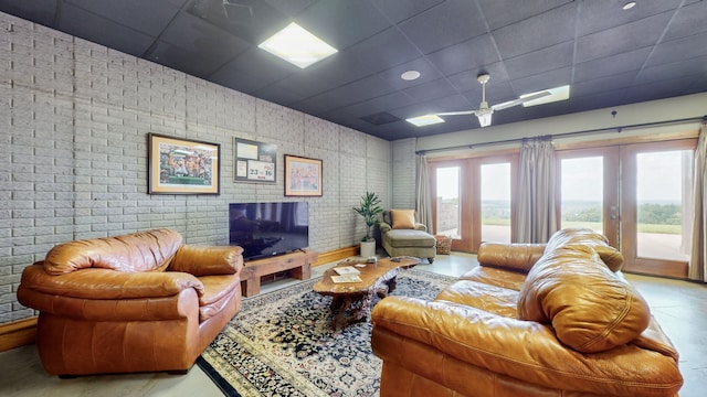 living room featuring a drop ceiling, brick wall, light tile floors, and french doors