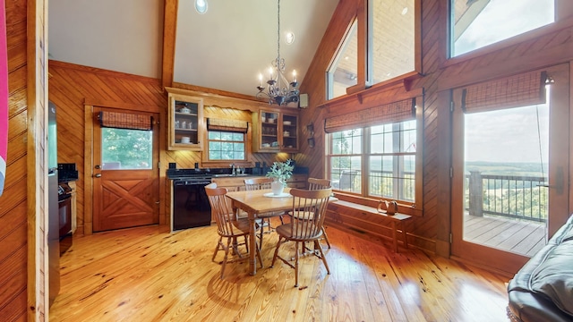 dining room featuring wooden walls, a chandelier, light hardwood / wood-style floors, and high vaulted ceiling