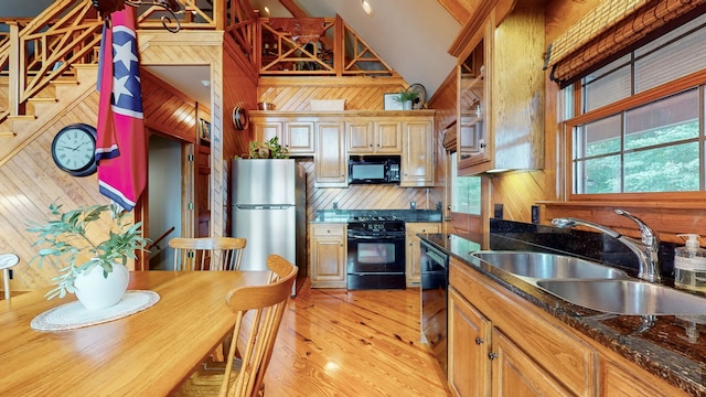 kitchen featuring dark stone counters, wooden walls, black appliances, light wood-type flooring, and sink