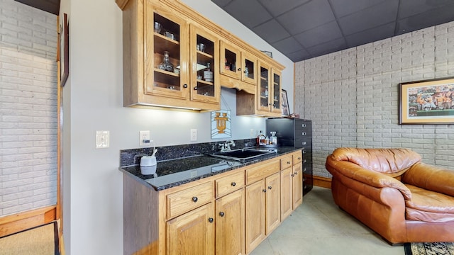 kitchen with a drop ceiling, brick wall, dark stone countertops, and sink