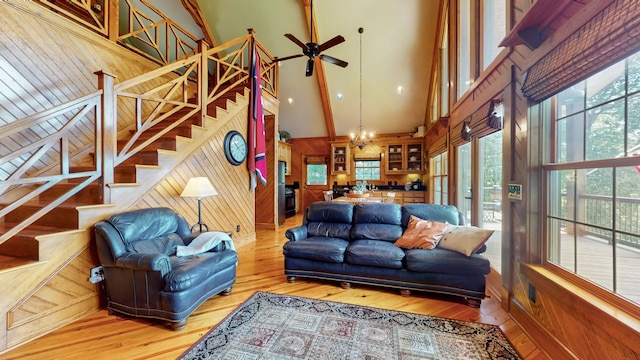 living room with light hardwood / wood-style flooring, wooden walls, ceiling fan with notable chandelier, and a towering ceiling