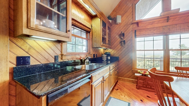 kitchen featuring wooden walls, sink, dark stone counters, light hardwood / wood-style flooring, and dishwasher