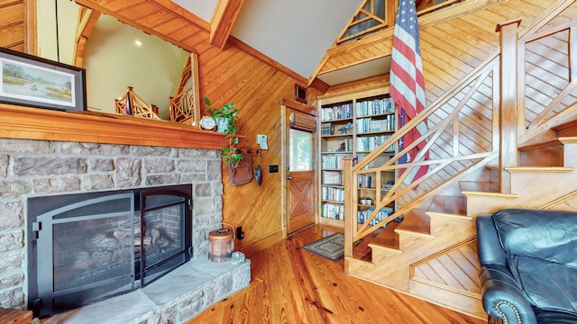 living room with a fireplace, wood walls, vaulted ceiling with beams, and hardwood / wood-style floors