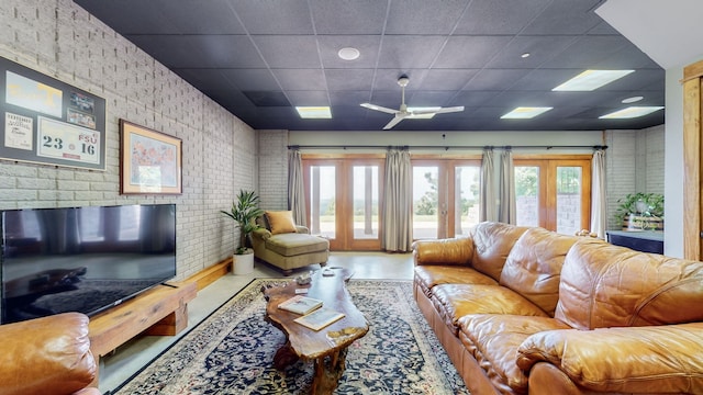 living room with a paneled ceiling, brick wall, ceiling fan, and french doors