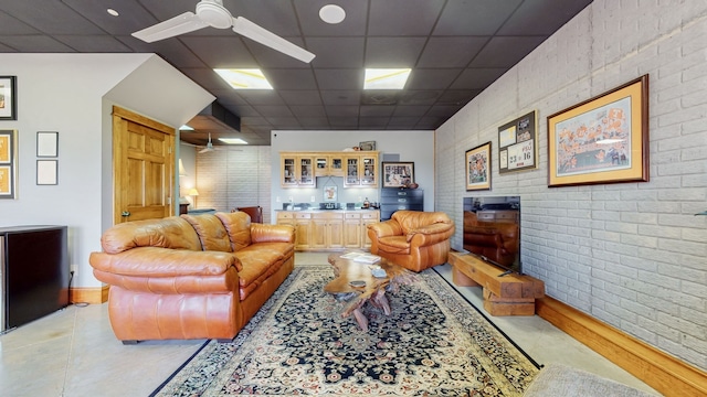 living room featuring ceiling fan, brick wall, and a paneled ceiling